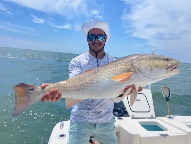 Smiling angler holding a large redfish aboard the Pathfinder
