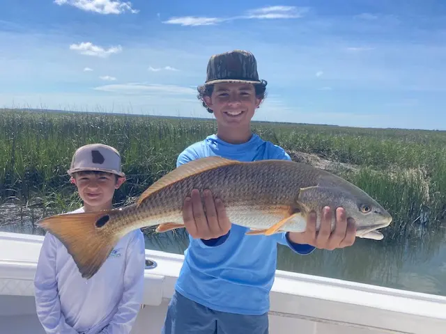 Two young anglers displaying a redfish in the salt marsh