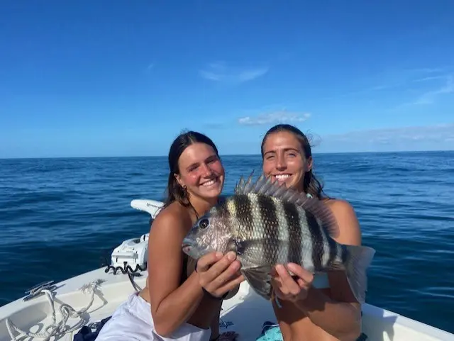 Two guests smiling with a sheepshead on a clear day