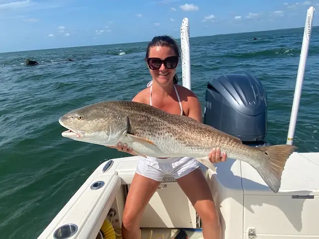 Guest holding a redfish beside the Pathfinder outboard