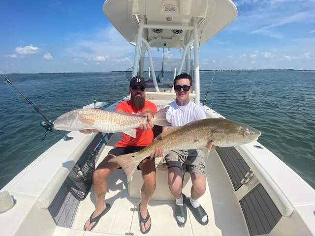 Two guests holding their catches at the bow of the boat